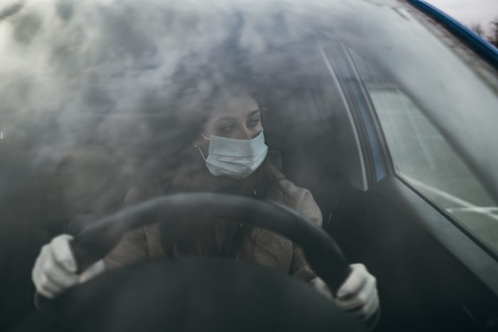 Young woman in a mask and gloves driving a car