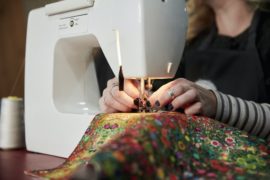A woman threading a needle on a sewing machine, sewing upholstery fabric.